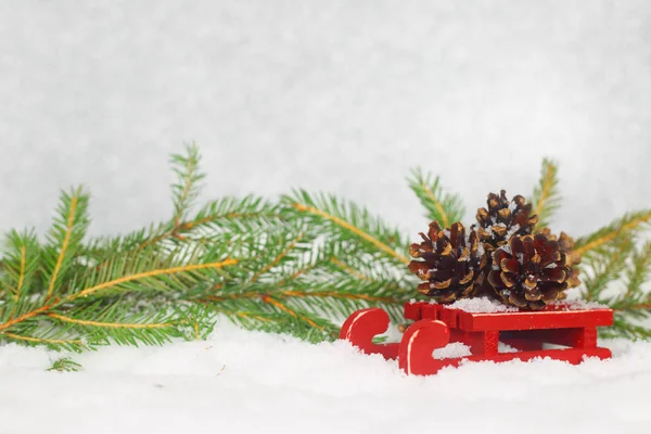 Tarjeta de Navidad con conos de pino en trineo de pie sobre la nieve con ramas de abeto — Foto de Stock