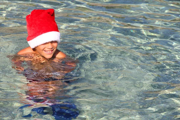 Lächelnder Junge mit Weihnachtsmütze im Meer — Stockfoto