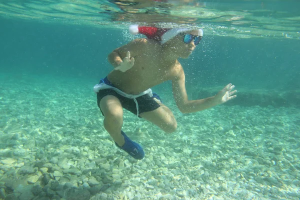Мальчик в шляпе Санты, купающийся в море — стоковое фото