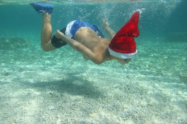 Chłopiec w Santa hat pływanie w morzu — Zdjęcie stockowe