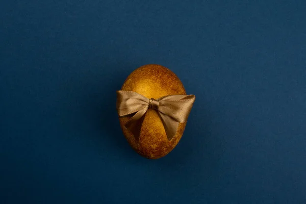 Ένα Μεγάλο Χρυσό Πασχαλινό Αυγό Κορδέλα Φιόγκο Μπλε Φόντο Αντίγραφο — Φωτογραφία Αρχείου