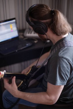 Müzik çalan sakallı müzisyen, oturma odasında otururken elektro gitar piyano ve dizüstü bilgisayarlı bir şarkı besteleyen Corona virüsü karantinası evde kalır.