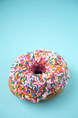 Pembe kremalı çörek ve mavi pastel arka planda şekerler.