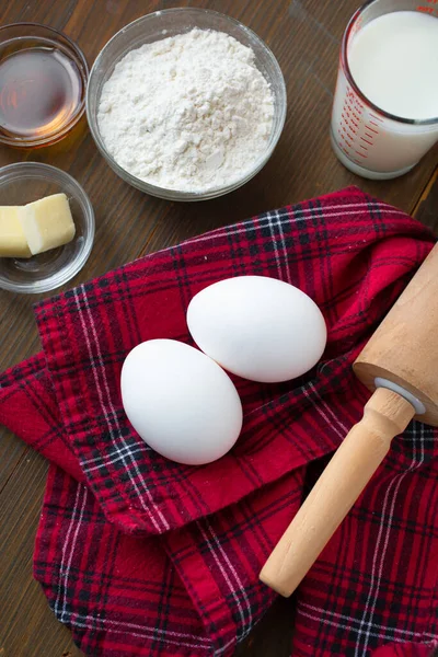 Ingredient for making delicious pancake ( eggs, flour, butter, milk with fresh maple syrup) on a red tablecloth and a rolling pin