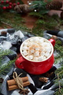 Marshmallow on top of a hot chocolate in a red cup surrounded by christmas candies, cinnamon and pine trees clipart