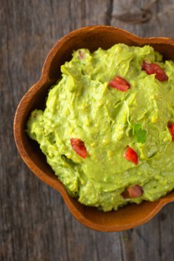 Tahta bir arka planda geleneksel Meksika guacamole kasesinin üst görüntüsü.