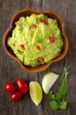 Tahta arka planda limonlu, domatesli, soğanlı ve kişniş soslu geleneksel Meksika guacamole tabağının en üst görüntüsü.