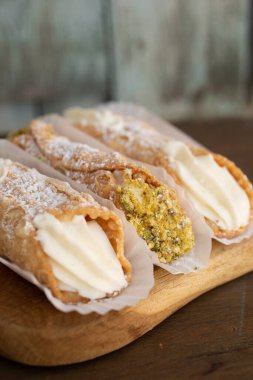 Üç İtalyan cannolis doğası ve ahşap arka planda bir dolapta şam fıstığı var.