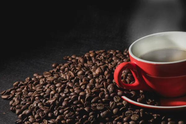 Sıcak kahve kırmızı Kupası ve kahve çekirdekleri arka plan vardır.