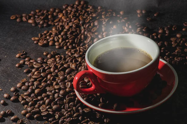 Warme koffie in rode kop en koffiebonen zijn de achtergrond. — Stockfoto