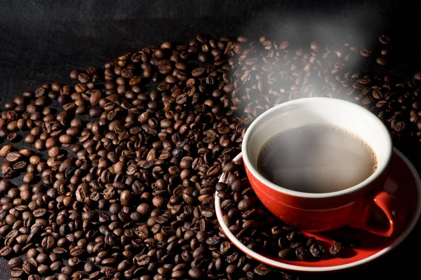 Warme koffie in rode kop en koffiebonen zijn de achtergrond. — Stockfoto