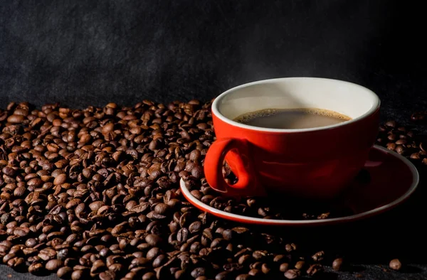 Warme koffie in rode kop en koffiebonen zijn de achtergrond. — Stockfoto