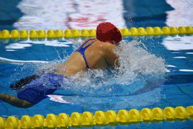 Açık havuzda yüzen, kelebek stilinde yüzen, nefes almak için heqd 'sini sudan çıkaran, ve koluyla kafasının üstünde, yandan ve yukarıdan bakan