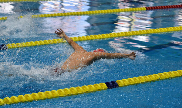 swimmer in a outdoor pool, swimming in a butterfly style, pulling his heqd out of the water to breathe, and with an arm raised above his head, side view and from above