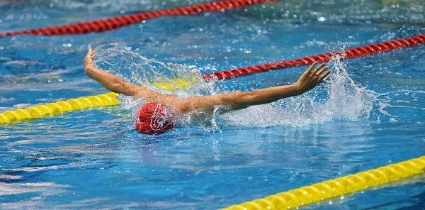 swimmer in a outdoor pool, swimming in a butterfly style, pulling his heqd out of the water to breathe, and with an arm raised above his head, side view and from above