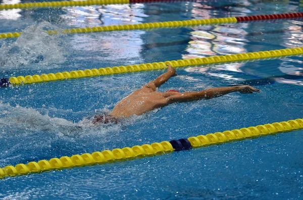 swimmer in a outdoor pool, swimming in a butterfly style, pulling his heqd out of the water to breathe, and with an arm raised above his head, side view and from above