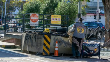 Kot ceketli evsiz bir adam çöpte kıyafet arıyor.