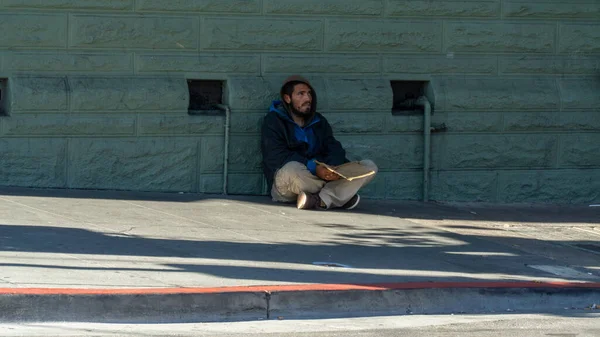 Hombre sin hogar con capucha sentado junto a la pared — Foto de Stock