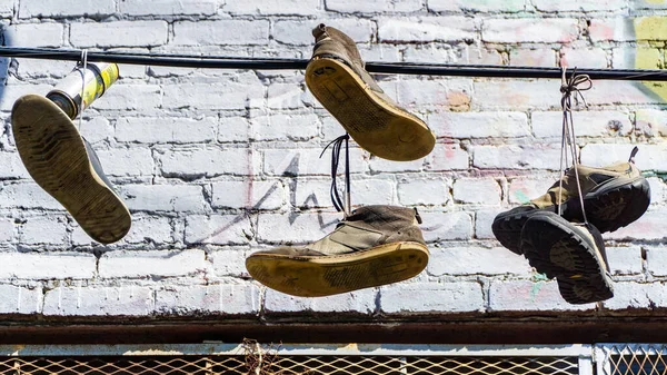 Primo piano di vecchie scarpe da ginnastica e scarpe appese a un filo davanti a un vecchio edificio — Foto Stock