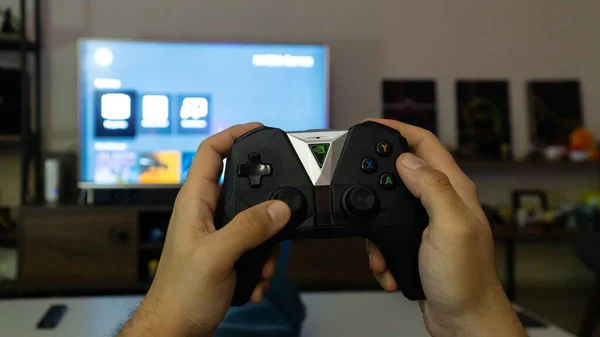 Cara com controlador Nvidia Shield com uma televisão em segundo plano — Fotografia de Stock