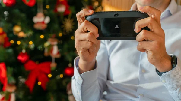 Mann spielt mit sony ps vita mit einem Weihnachtsbaum im Rücken — Stockfoto