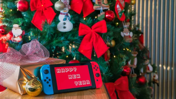 Nintendo Switch mit frohem neuen Jahr auf dem Bildschirm mit einem Weihnachtsbaum im Hintergrund — Stockfoto