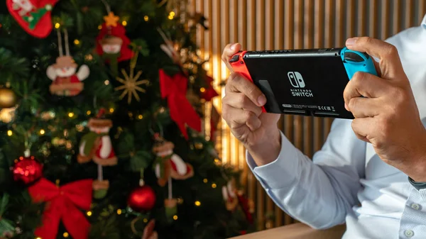 Hombre jugando con Nintendo Switch con un árbol de navidad Fotos de stock