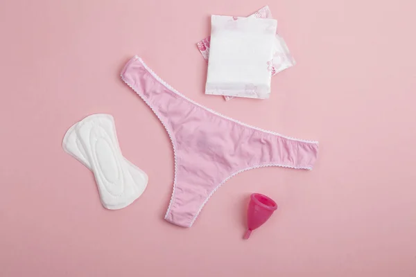Farklı tipte kadın hijyen ürünleri, regl bardakları, hijyenik pedler ve tamponlar. Pembe kadın külotu, hijyenik peçeteler, tamponlar, pembe arka planda regl kupası. Adet görme kavramı. 
