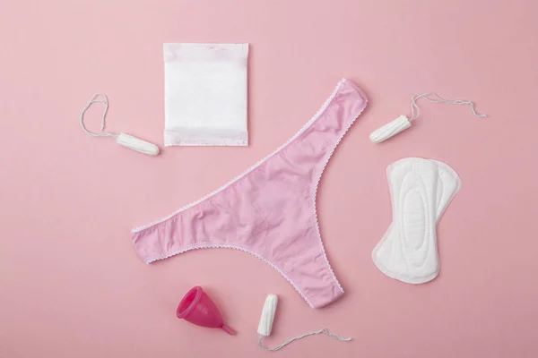 Farklı tipte kadın hijyen ürünleri, regl bardakları, hijyenik pedler ve tamponlar. Pembe kadın külotu, hijyenik peçeteler, tamponlar, pembe arka planda regl kupası. Adet görme kavramı. 