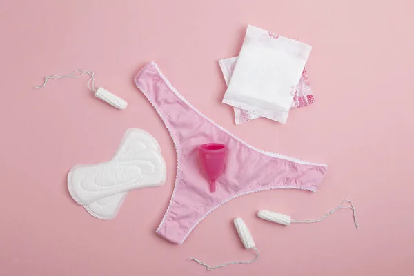 Farklı tipte kadın hijyen ürünleri, regl bardakları, hijyenik pedler ve tamponlar. Pembe kadın külotu, hijyenik peçeteler, tamponlar, pembe arka planda regl kupası. Adet görme kavramı. 