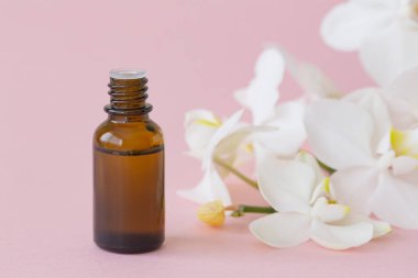 Masaj yağı ve pembe arka planda beyaz orkide. Güzellik konsepti, doğal kozmetik ürünler. Orkide özü, aromatik yağlar. Boşluğu kopyala.