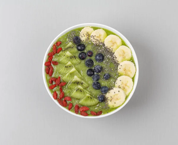 Healthy breakfast smoothie bowl topped with blueberry, kiwi, banana, spinach, Chia seeds and Goji berries. Detox concept. Green smoothie bowl on grey background. Top view.