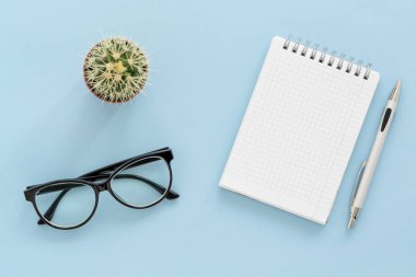 Not defteri, kalem, bardak ve mavi arka planda kahve fincanı olan serbest bir iş yeri. Düz yatıyordu. Kopyalama alanı olan üst görünüm.  