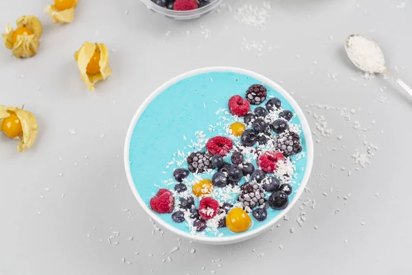 Breakfast smoothie bowl with blue spirulina, yogurt, raspberries, blueberries, Blackberries, physalis and coconut flakes. Detox smoothie bowl. Vegan food.