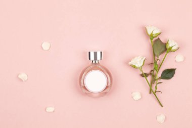 Pembe arka planda beyaz güller olan bir şişe parfüm. Düz konum, üst görünüm, kopyalama alanı. 