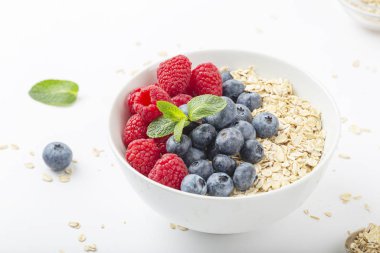 Kahvaltılık smoothie kasesi granola, taze ahududu, yabanmersini ve beyaz zemin üzerinde nane. Sağlıklı yemek..