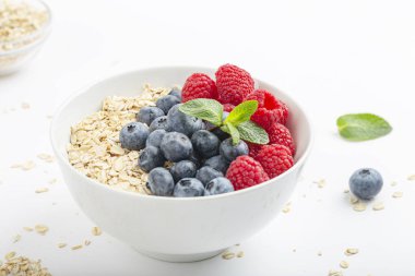 Kahvaltılık smoothie kasesi granola, taze ahududu, yabanmersini ve beyaz zemin üzerinde nane. Sağlıklı yemek..