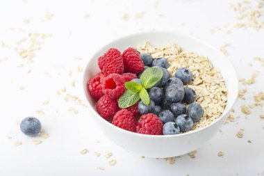 Kahvaltılık smoothie kasesi granola, taze ahududu, yabanmersini ve beyaz zemin üzerinde nane. Sağlıklı yemek..