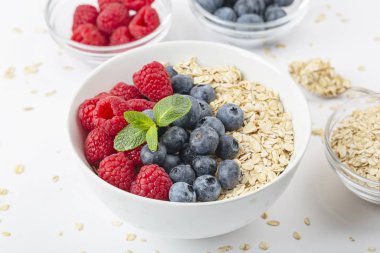 Kahvaltılık smoothie kasesi granola, taze ahududu, yabanmersini ve beyaz zemin üzerinde nane. Sağlıklı yemek..