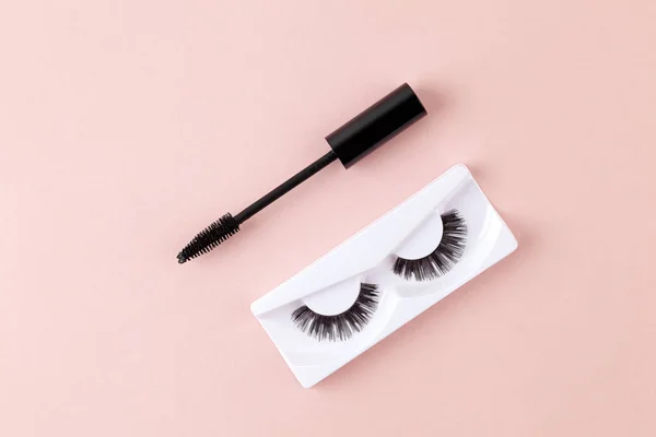 Women's eyelashes and brush on a pink background. Top view of Mascara brush and long false lashes. Eyelash extension, beauty blog concept.