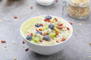 Kahvaltı kivili smoothie kasesi yulaf gevreği ve böğürtlenli. Muz, Goji üzümü, yabanmersini, Chia tohumu, hindistan cevizi ve müsli ile lezzetli kivili smoothie. Vejetaryen yemeği. 