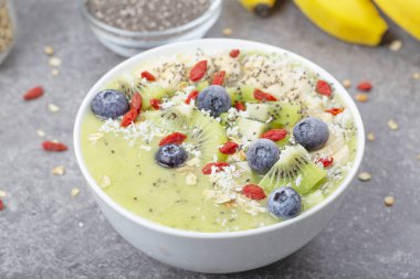 Kahvaltı kivili smoothie kasesi yulaf gevreği ve böğürtlenli. Muz, Goji üzümü, yabanmersini, Chia tohumu, hindistan cevizi ve müsli ile lezzetli kivili smoothie. Vejetaryen yemeği. 