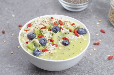 Kahvaltı kivili smoothie kasesi yulaf gevreği ve böğürtlenli. Muz, Goji üzümü, yabanmersini, Chia tohumu, hindistan cevizi ve müsli ile lezzetli kivili smoothie. Vejetaryen yemeği. 
