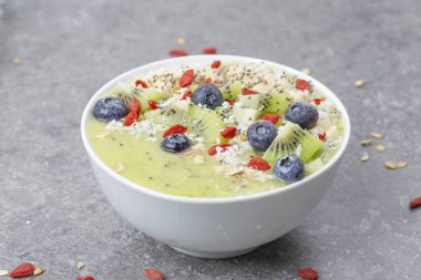 Kahvaltı kivili smoothie kasesi yulaf gevreği ve böğürtlenli. Muz, Goji üzümü, yabanmersini, Chia tohumu, hindistan cevizi ve müsli ile lezzetli kivili smoothie. Vejetaryen yemeği. 