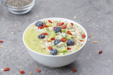 Kahvaltı kivili smoothie kasesi yulaf gevreği ve böğürtlenli. Muz, Goji üzümü, yabanmersini, Chia tohumu, hindistan cevizi ve müsli ile lezzetli kivili smoothie. Vejetaryen yemeği. 