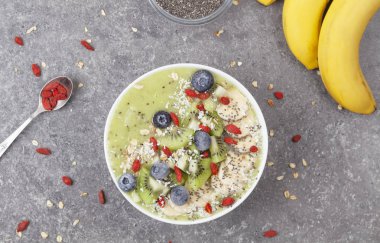 Kahvaltı kivili smoothie kasesi yulaf gevreği ve böğürtlenli. Muz, Goji üzümü, yabanmersini, Chia tohumu, hindistan cevizi ve müsli ile lezzetli kivili smoothie. Vejetaryen yemeği. 