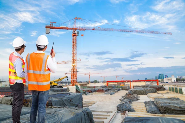 Ingenieur und Polier beim Blick auf den Kranbau mit Gesprächen auf dem Walkie-Talkie zur Steuerung der Kranbeladung auf der Baustelle — Stockfoto