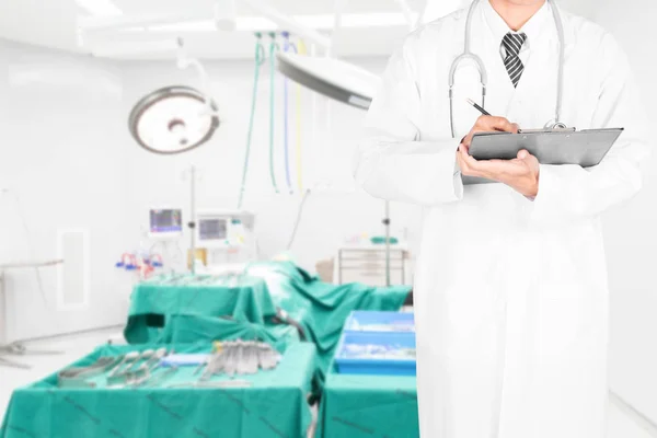 Medico scrivere qualcosa negli appunti per la diagnosi con una sala operatoria sullo sfondo — Foto Stock