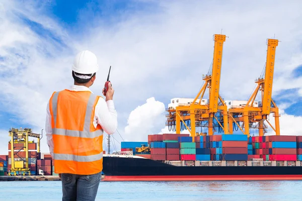 Dock worker talking on the walkie-talkie for controlling loading container in an industrial harbor