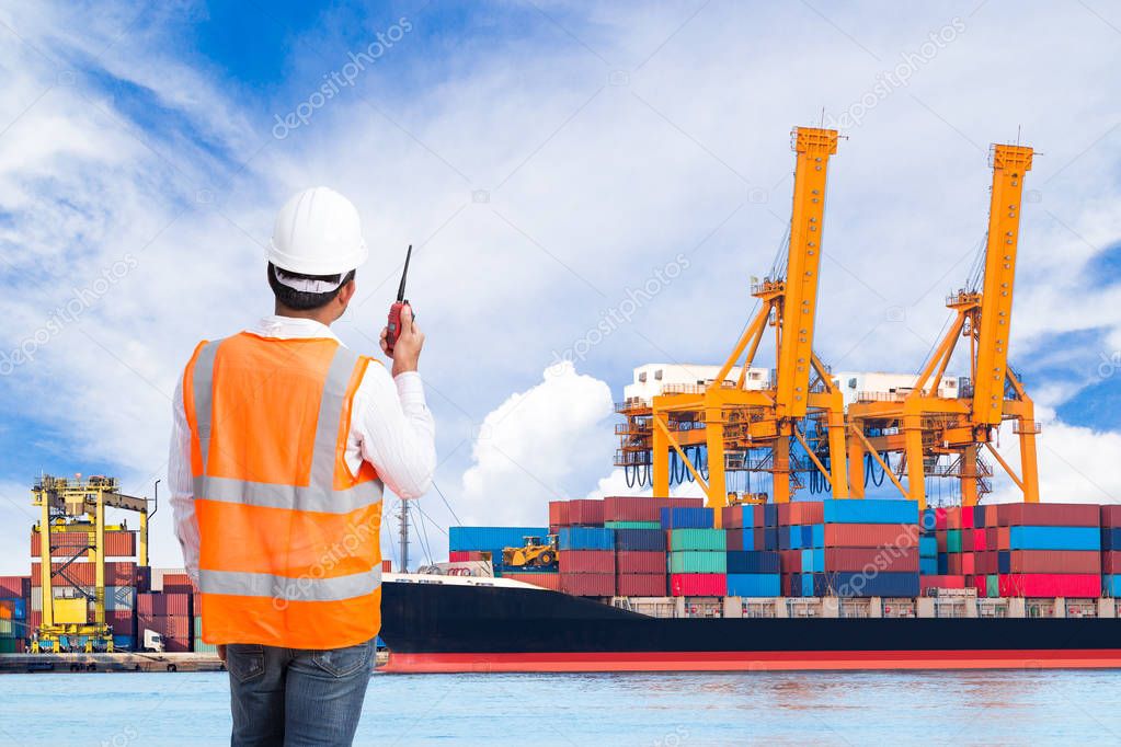 Dock worker talking on the walkie-talkie for controlling loading container in an industrial harbor